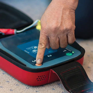 A hand pressing a button on an AED machine